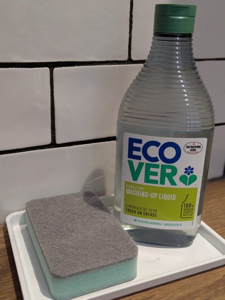 Basics provided Ecover cleaning product bottle next to a cleaning sponge on a tray.