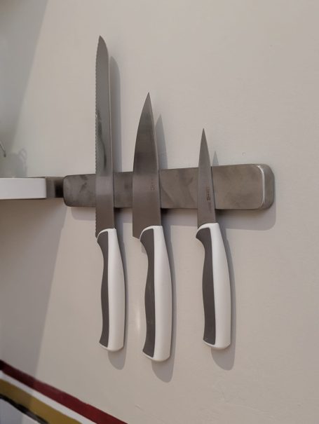 Knives Four kitchen knives with white handles mounted on a metal strip against a wall.