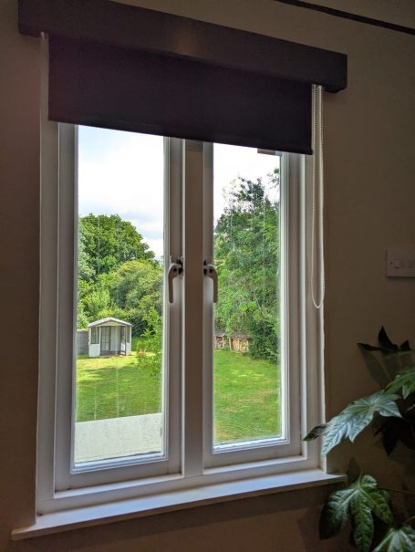 A room with a garden view A view through a window showing a garden with greenery and a shed.