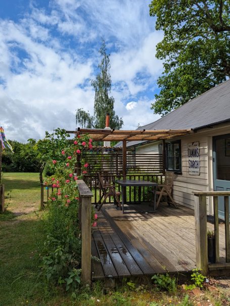Garden View A wooden deck with seating, surrounded by greenery and flowers under a blue sky.