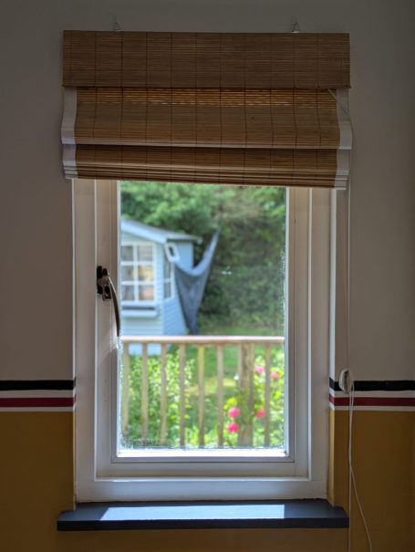 Garden view A window with a wooden blind overlooking a garden and adjacent house.