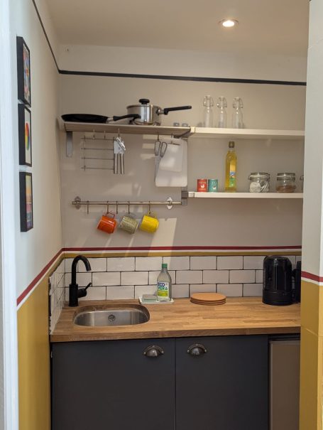 Kitchenette Compact kitchen area featuring a sink, shelves, mugs, and various kitchenware.