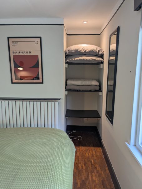 Cosy bedroom with shelving Cozy bedroom corner with a bed, shelving unit, and light wood flooring.