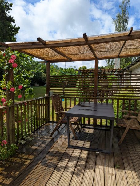 Private & Peaceful Outdoor Seating A wooden deck with a table and chairs, shaded by a bamboo canopy, surrounded by greenery.